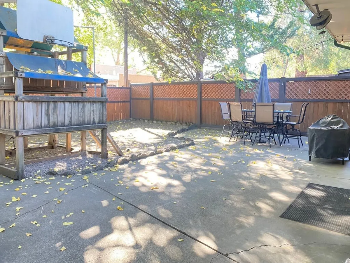 This image features a play structure and a spacious patio area with an outdoor dining table, all set within a well-kept backyard. The scene is relaxed and welcoming, ideal for family meals, evening gatherings, and supervised children’s play.