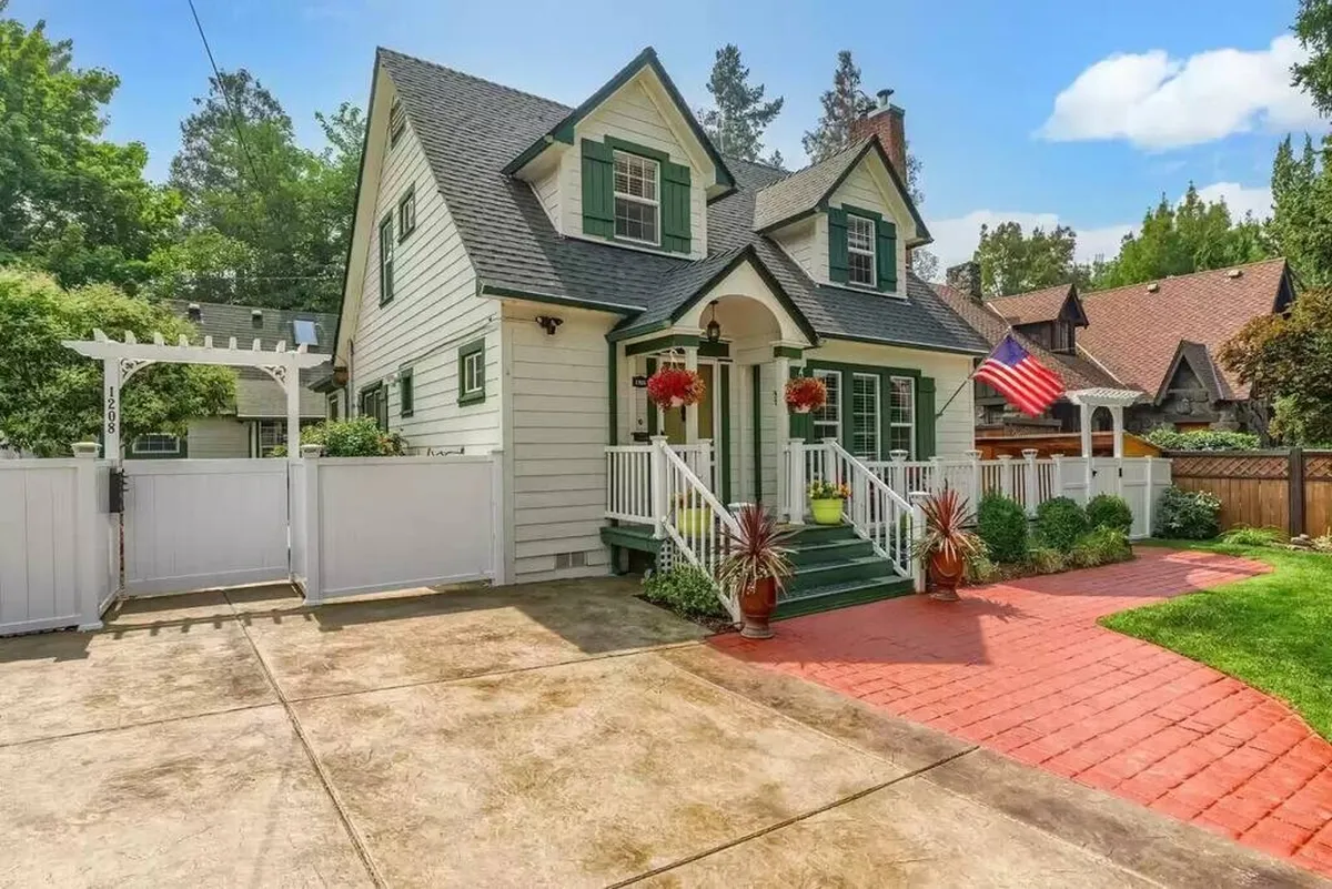This exterior image showcases the front entrance of the home, beautifully framed by lush greenery, decorative planters, and an American flag. The inviting porch area suggests a welcoming environment, perfect for groups arriving together or gathering before heading out to explore downtown.