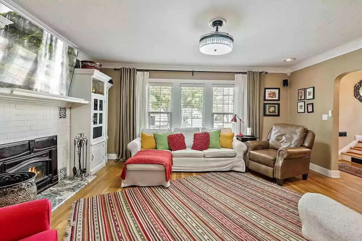 A sunlit living area showcasing an elegant fireplace, a large sofa and armchair, soft rugs, and bright windows. The period details and welcoming layout create a sophisticated yet comfortable ambiance, ideal for relaxing after a day of exploring.