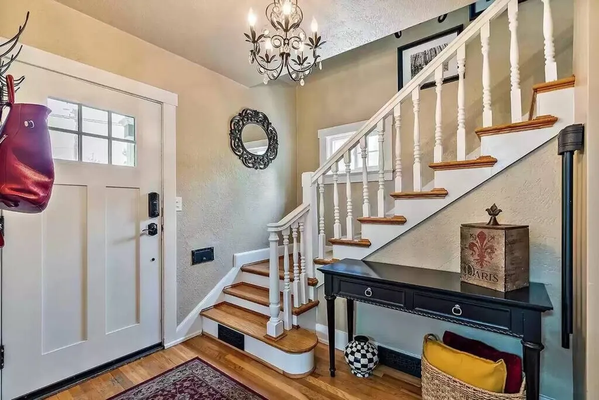 An inviting interior entryway scene featuring a chandelier, staircase, front door, and a console table with decor. The space feels open and ready to greet guests, highlighting the home's friendly and welcoming vibe for arriving groups or families.