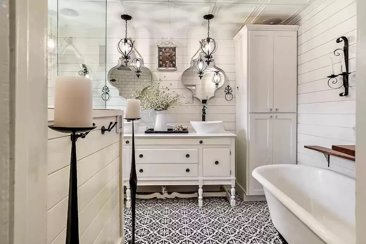 The image showcases a serene bathroom featuring a freestanding bathtub beneath elegant decorative lighting, flanked by ornate mirrors. Soft natural light fills the space, highlighting the luxurious and calming atmosphere perfect for relaxation and self-care.