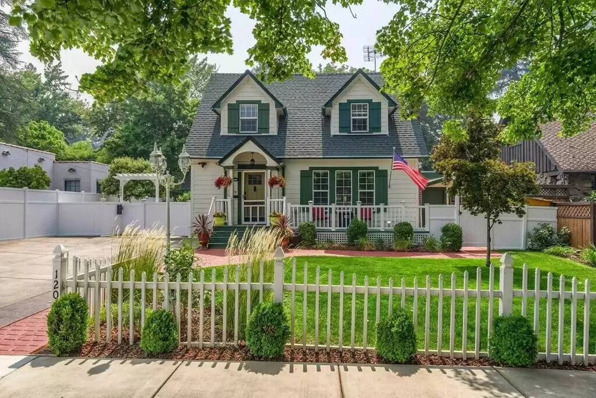 The front of the home features a classic white picket fence, landscaped garden, and roomy lawn, with the American flag waving beside the door. The yard offers ample space for children to play and for families to host casual gatherings or socialize with neighbors.